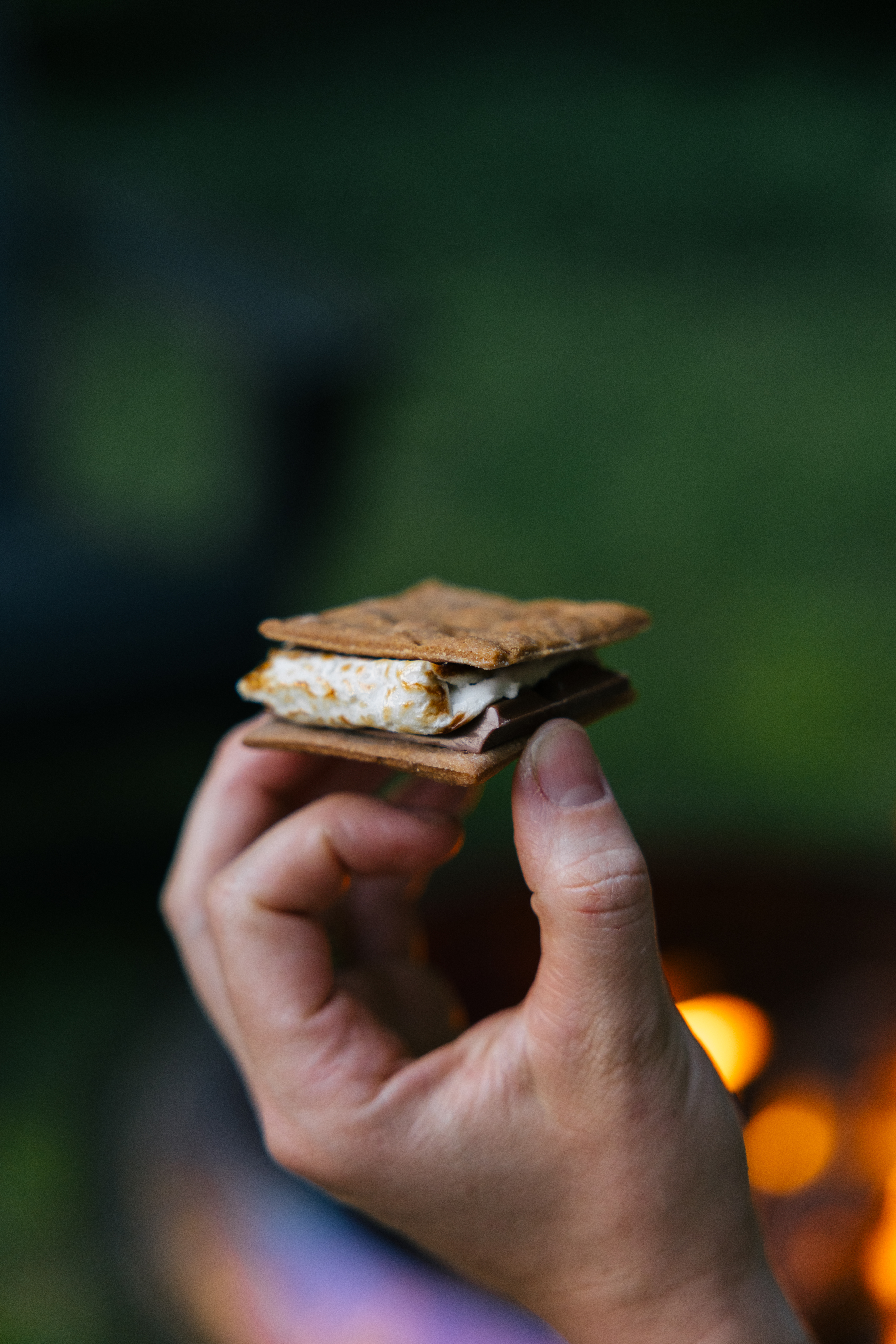 Hand holding a toasted s’more near an outdoor fire